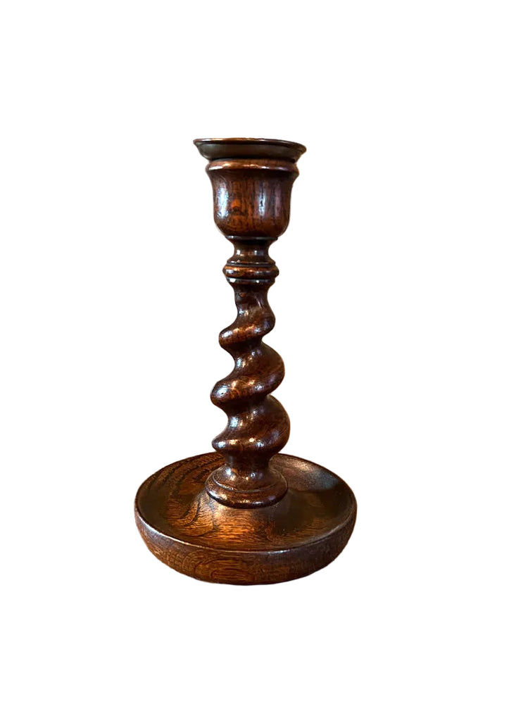 Wooden candlestick on a wooden surface with framed artwork in the background