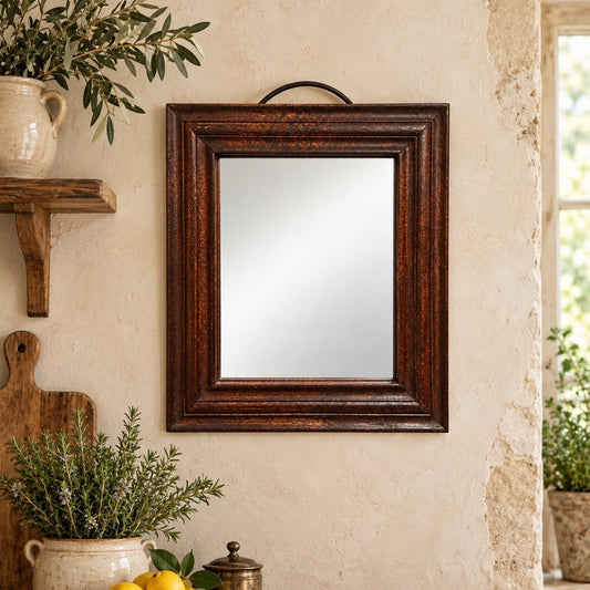 A rectangular wall mirror with a dark brown wooden frame hangs on a textured beige wall above a rustic wooden console table decorated with plants, lemons, and a small brass jar.
