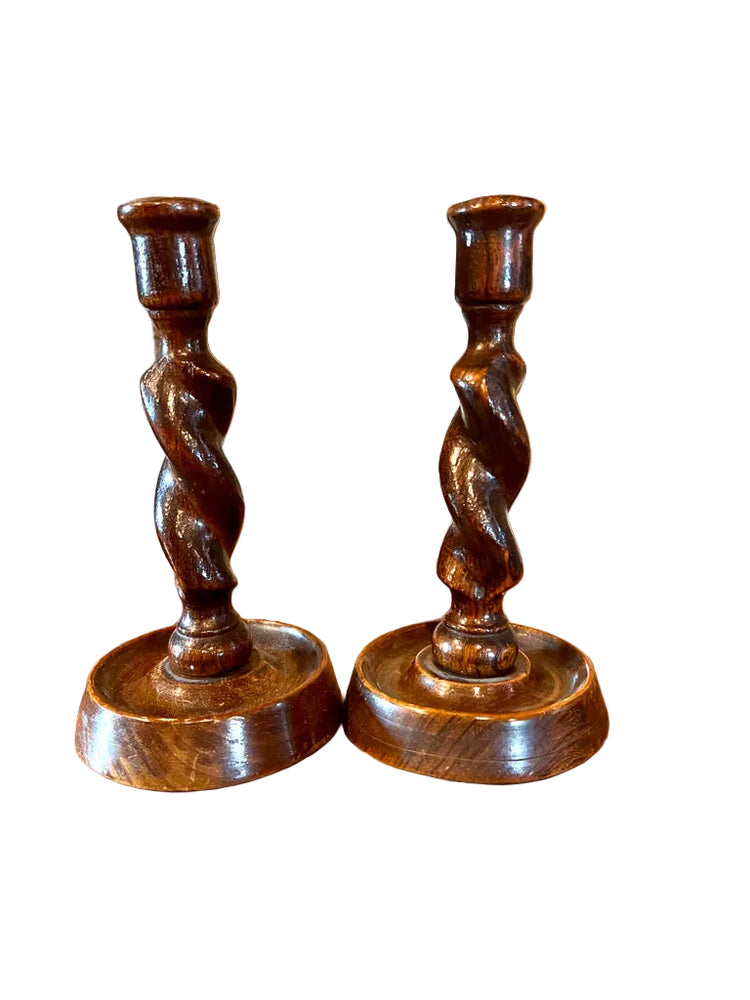 Pair of wooden candlesticks on a wooden surface with framed pictures in the background.