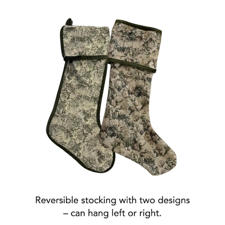 Two reversible fabric stockings with a floral and botanical pattern in beige, brown, and green tones, shown on a light gray background with text below stating 'Reversible stocking with two designs – can hang left or right.'.
